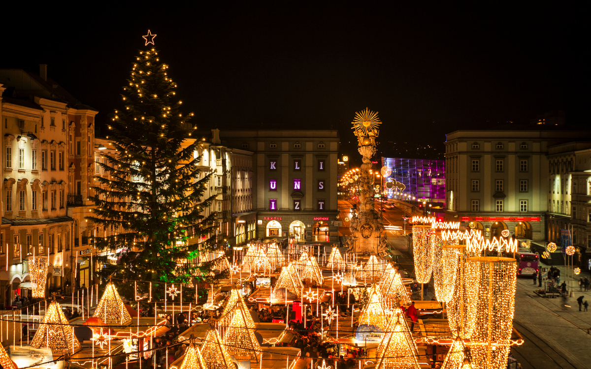Weihnachtsmarkt in der Stadt bei Nacht mit festlicher Beleuchtung und Christbaum.