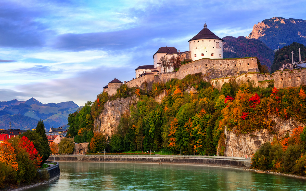 Festung auf einem Hügel am Fluss, umgeben von Herbstbäumen.