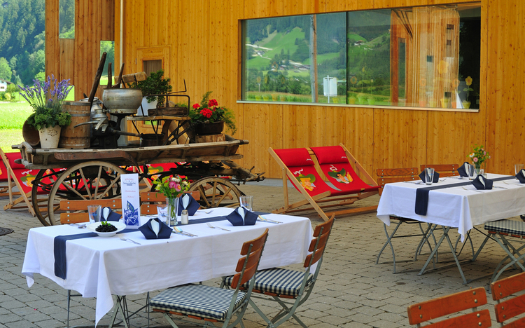 Restaurantterrasse mit gedeckten Tischen und dekorativem Wagen im Freien.