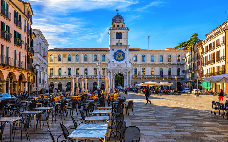 Historisches Gebäude mit Turm und Uhr in einer sonnigen, leeren Piazza.
