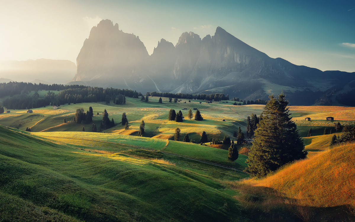 Malerische Berglandschaft bei Sonnenaufgang mit grünen Wiesen und Bäumen.