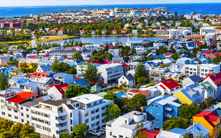 Stadtpanorama mit bunten Häusern, Bäumen und einem See im Hintergrund.