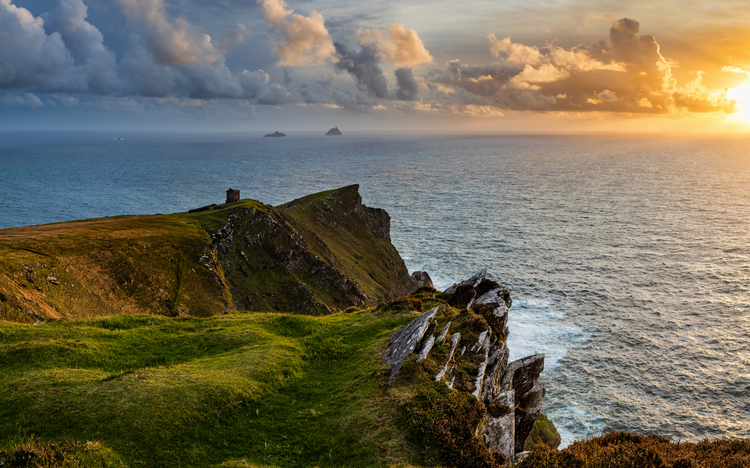 Klippenlandschaft am Meer bei Sonnenuntergang, Wolken am Horizont.