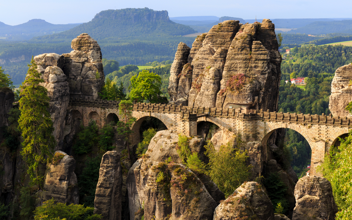 Eine steinerne Brücke zwischen Felsformationen in einer bewaldeten Landschaft.