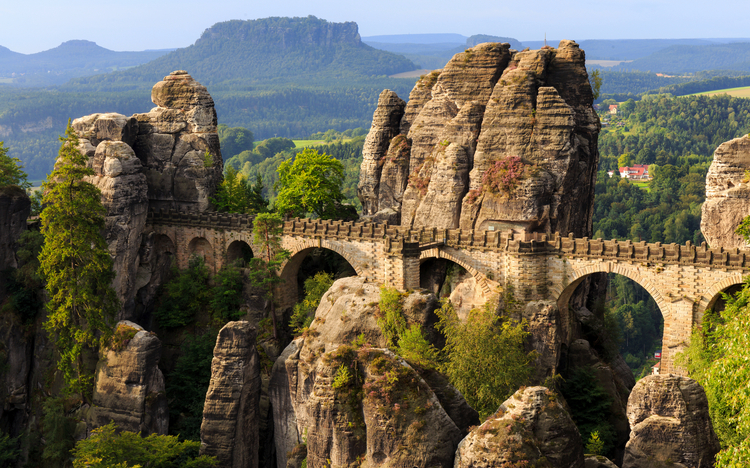 Eine steinerne Brücke zwischen Felsformationen in einer bewaldeten Landschaft.